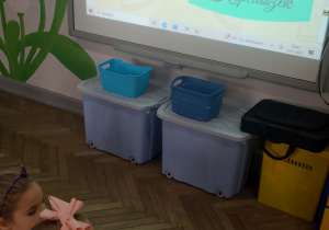 Dzieci siedzą na dywanie przed tablicą interaktywną i rozwiązują "Bajkowe zagadki".