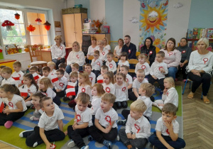Dzieci z innych grup oraz pracownicy przedszkola siedzą na widowni i oglądają przedstawienie z okazji Święta Niepodległości.