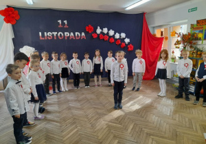 Na środku sceny stoi Antoś i recytuje wiersz zapraszając wszystkich do zaśpiewania hymnu narodowego.