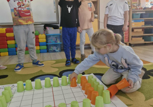 Alicja układa pomarańczowe kubeczki na macie do kodowania.