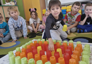 Wojtuś układa kubeczki na macie do kodowania tworząc jesienne drzewo.