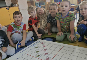 Dzieci na dużej macie do kodowania układają jesienne liście według podanego kodu.