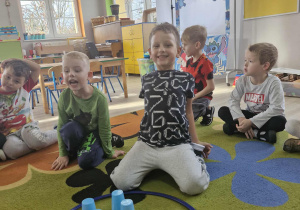 Lucjan i Franuś siedzą przed niebieskim okręgiem, w którym znajdują się kostka z czterema kropkami i cztery niebieskie kubki.