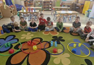 Na środku dywanu rozłożone są cztery okręgi, a w nich kostki do gry i kolorowe kubeczki.