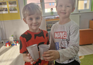 Olek i Julek trzymają w dłoniach szare kubeczki.