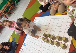 Na dywanie rozłożona jest mata do kodowania. Hania ułożyła pień drzewa z kubeczków.