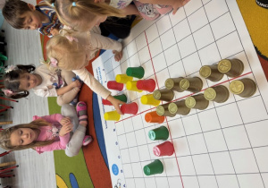 Dzieci tworzą koronę drzew z kubeczków w kolorach zielonym, żółtym pomarańczowym i czerwonym. Na zdjęciu Kornelia układa czerwony kubeczek.