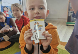 Lucjan trzyma w dłoniach karteczkę z napisem Bunia oraz z wizerunkiem bajkowego Gumisia.