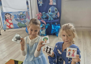 Oliwia i Ala trzymają w dłoniach bajkowe obrazki i pasujące do nich cienie.