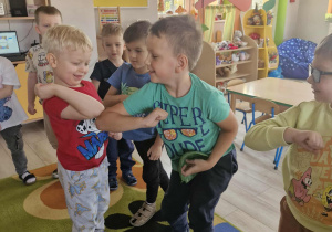 Karol i Franek dotykają się łokciami. W tle widać przyglądające się temu dzieci.