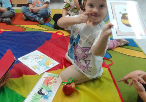 Hania prezentuje wylosowany obrazek - garnek miodu. Obok siedzą dzieci z grupy.