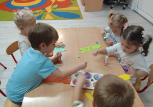Dzieci przy stolikach naklejają gotowe elementy na zakładki do książki.