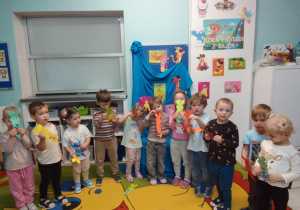 "Pszczółki" prezentują wykonane przez siebie kolorowe zakładki do książki. Dzieci stoją na tle dekoracji z napisem "Dzień postaci z bajek".