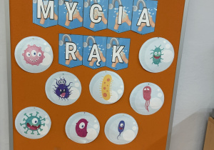 Niebieski napis "Światowy Dzień Mycia Rąk" na pomarańczowym tle, pod napisem fotografie wirusów.