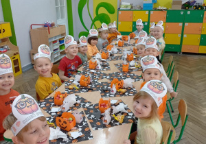 Grupka dzieci podczas słodkiego poczęstunku, na stole są serwetki w dynie oraz pudełeczka kolorowe z łakociami.