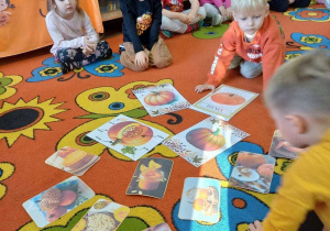 Grupka dzieci na dywanie ogląda dynie na fotografiach.