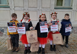 Dzieci stoją na chodniku i pozują do zdjęcia z otrzymanymi dyplomami i nagrodami.