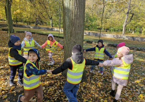 Dzieci trzymając się za ręce radośnie tańczą wokół drzewa