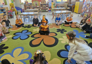 Dzieci siedzą w kole na dywanie. Po środku siedzi Lucjan przebrany za dyniowego Czarodzieja