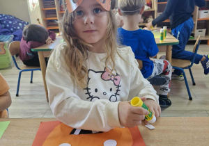 Weronika siedzi przy stoliczku i wykleja papierową dynię