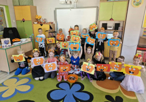 Biedronki ustawione pod tablicą multimedialną pokazują do zdjęcia wykonane przez siebie dyniowe prace plastyczne