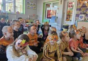 Przedszkolaki w dyniowych maskach siedzą na dywanie i oglądają film edukacyjny