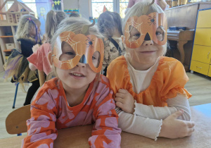 Zuzia i Nadia siedzą przy stoliku w dyniowych maskach