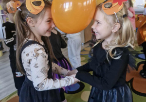 Oliwia Ko. i Ala w trakcie dyniowego tańca. Dziewczynki trzymają głowami pomarańczowy balon