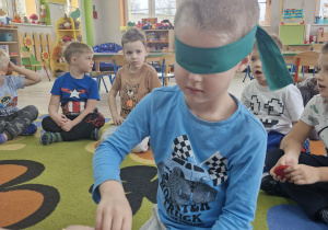 Julek z zasłoniętymi szarfą oczami wyjmuje z woreczka figurę geometryczną.