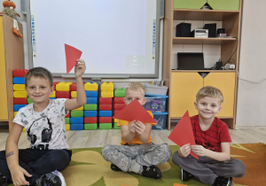 Franek, Lucjan i Olek siedzą na dywanie. Chłopcy trzymają w dłoniach czerwone trójkąty.
