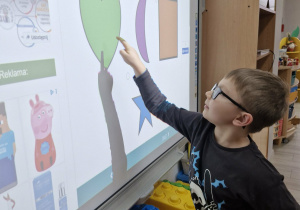 Tymek stojąc przy tablicy multimedialnej klika w kształt zielonego serca.