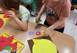 Chłopcy przyklejają elementy figur geometrycznych na kartki.