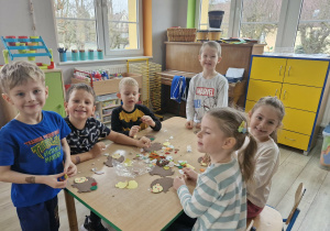 Grupa dzieci siedząc przy stoliku tworzy pracę plastyczną z wizerunkiem jeża.