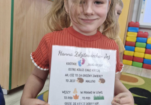 Weronika trzyma w dłoniach historyjkę obrazkową z wierszem „Jeż”.