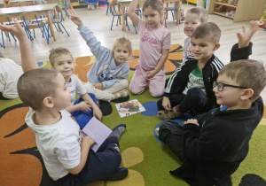 Grupa dzieci siedząc na dywanie układa puzzle z wizerunkiem jeża.