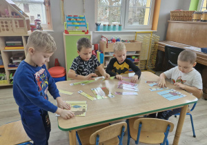 Olek, Franek, Lucjan i Szymek układają przy stoliku pocięte na części obrazki z jeżami.