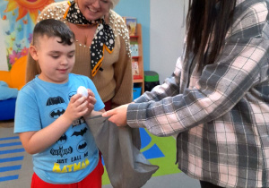 Jakub wrzuca do worka znalezione jajko. Obok chłopca stoi Pani Agata i jej córka.