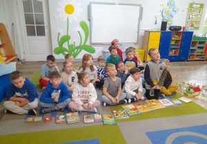 Dzieci siedzą na dywanie, a przed nimi leżą książki o wsi. Obok stoi zagroda wiejska ustawiona z figurek.