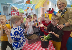 Grupka dzieci po zabawie w "kopanie ziemniaków" podnosi do góry ręce ubrudzone w ziemi. Obok stoi Pani Agata.