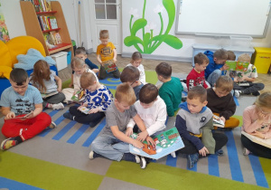 Dzieci siedzą na dywanie i oglądają książki.