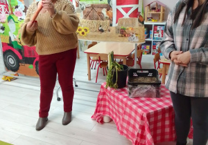 Pani Agata i jej córka prezentują dzieciom warzywa z pola i z ogrodu. Obok stolik, na którym leżą warzywa