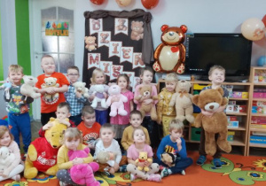 Grupa "Motylków" z e swoimi misiami pozuje do zdjęcia na tle dekoracji Dzień Misia.