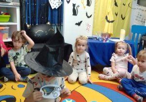 Leon wylosował gwiazdkę, pod którą jest obrazek z zawodem policjanta. W tle dekoracja andrzejkowa. Inne dzieci z zaciekawieniem obserwują działania kolegi.