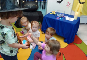 Michał w w halloweenowej czapce rozdaje ze szkatułki karteczki z imionami.