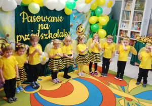 Dzieci stoją w półkolu i mówią wierszyk z pokazywaniem.