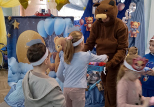 Nauczyciel w stroju misia wręcza dzieciom misiowe upominki.