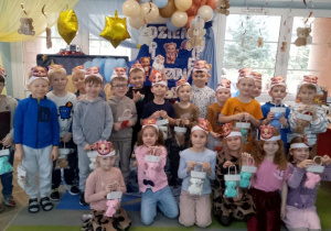 Zdjęcie grupowe dzieci z otrzymanymi upominkami na tle dekoracji.