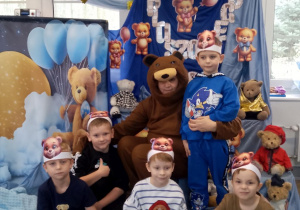 Grupka chłopców wspólnie z nauczycielem w stroju misia pozują na tle dekoracji.