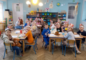 Dzieci siedzą przy stolikach i wykonują misiową pracę plastyczną.