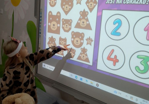 Dziewczynka na tablicy liczy misie.